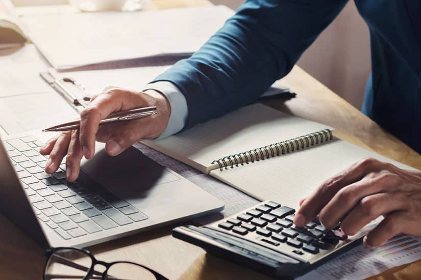 tax professional working on voluntary disclosure program using calculator with laptop desk